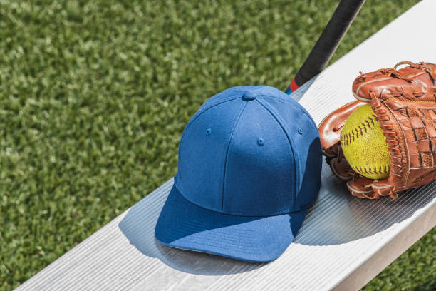 istock A blue baseball cap with a yellow softball in glove and bat on bench 938307358