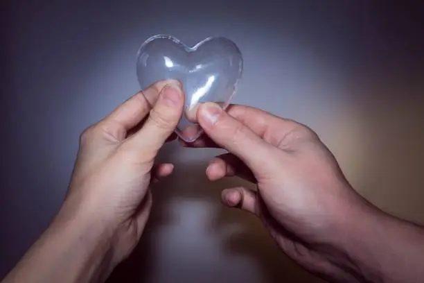 two hands holding a transparent glass heart