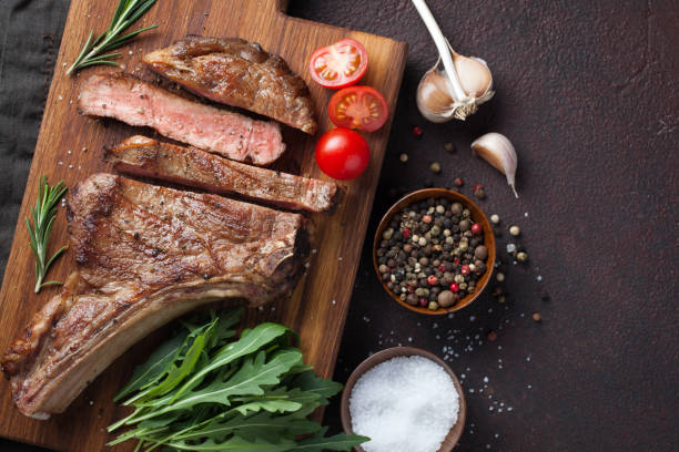 istock Grilled cowboy beef steak, herbs and spices on a dark stone background. Top view with copy space for your text 938332842