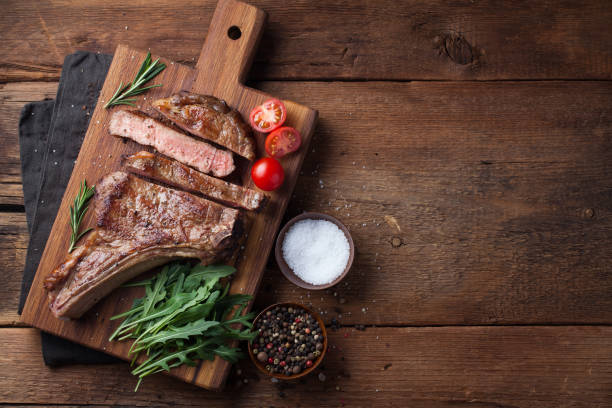 bife grelhado vaqueiro, ervas e especiarias em um fundo de madeira rústica. vista superior com espaço de cópia para o seu texto - rib eye steak beef cutting board meat - fotografias e filmes do acervo