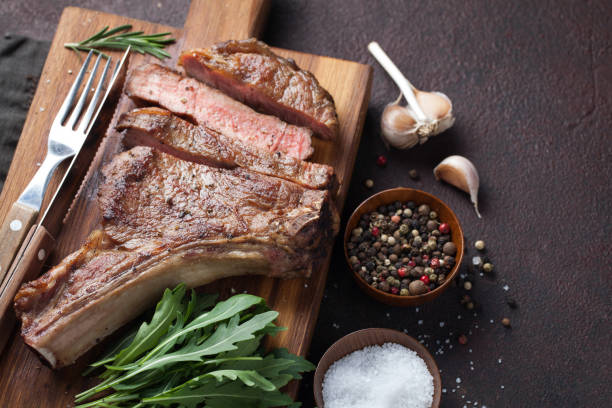 istock Grilled cowboy beef steak, herbs and spices on a dark stone background. Top view 938332872