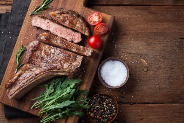 istock Grilled cowboy beef steak, herbs and spices on a rustic wooden background. Top view with copy space for your text 938332884
