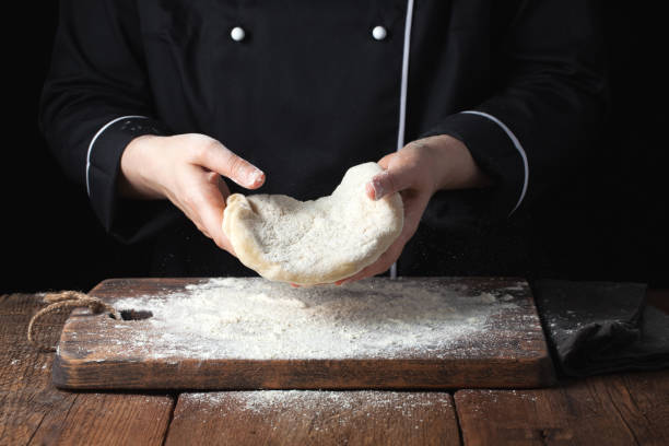 istock Female chef holding yeast dough in her hands on black background 938332906
