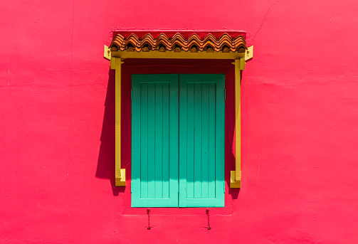 Pink wall with teal window shutter
