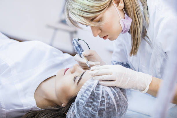 istock Beautician female applies permanent makeup on eyebrows, tattoo eyebrows on beautiful models in a beauty parlor 938368034