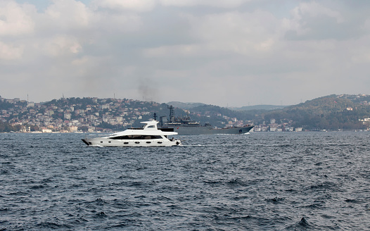 Yacht and war ship cross Bosphorus strait in Tarabya area of Istanbul.