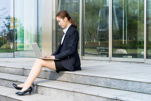 istock young woman in formalwear using laptop outside office building 938384376