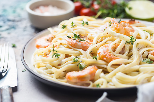 Italian pasta fettuccine in a creamy sauce with shrimp on a plate, close-up.