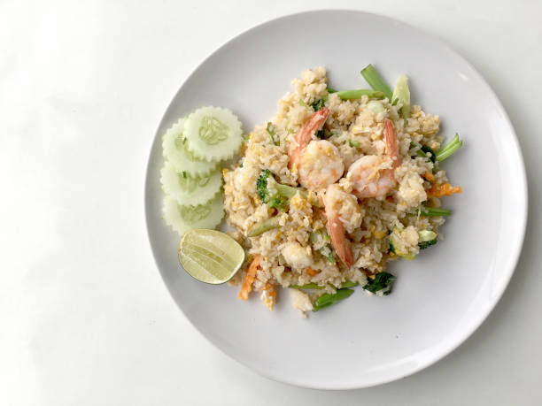 istock Fried rice with prawn herbs and vegetables served with lemon and cucumber in white plate on white background. Part of a series of nine Asian food dishes. Thai Food. 938387888