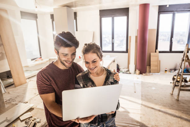 istock Happy embraced couple using laptop while being on construction site in their apartment. 938388400