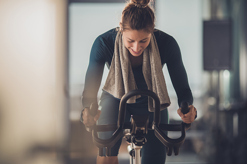 Happy athletic woman cycling on exercise bike in a gym.