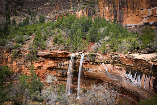 a hiking trail goes under a waterfall in a sandstone canyon