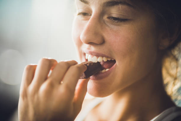 Close up of a happy woman eating chocolate. Close up of young beautiful woman biting chocolate candy. chocolate bar stock pictures, royalty-free photos & images