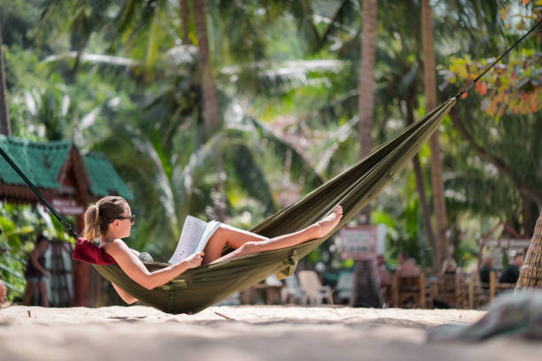 istock Relaxed woman sunbathing in hammock on the beach and reading a book. 938395736