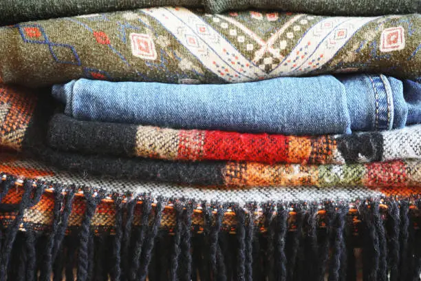 Photo of Stack of warm clothes of different patterned fabrics in boho style.