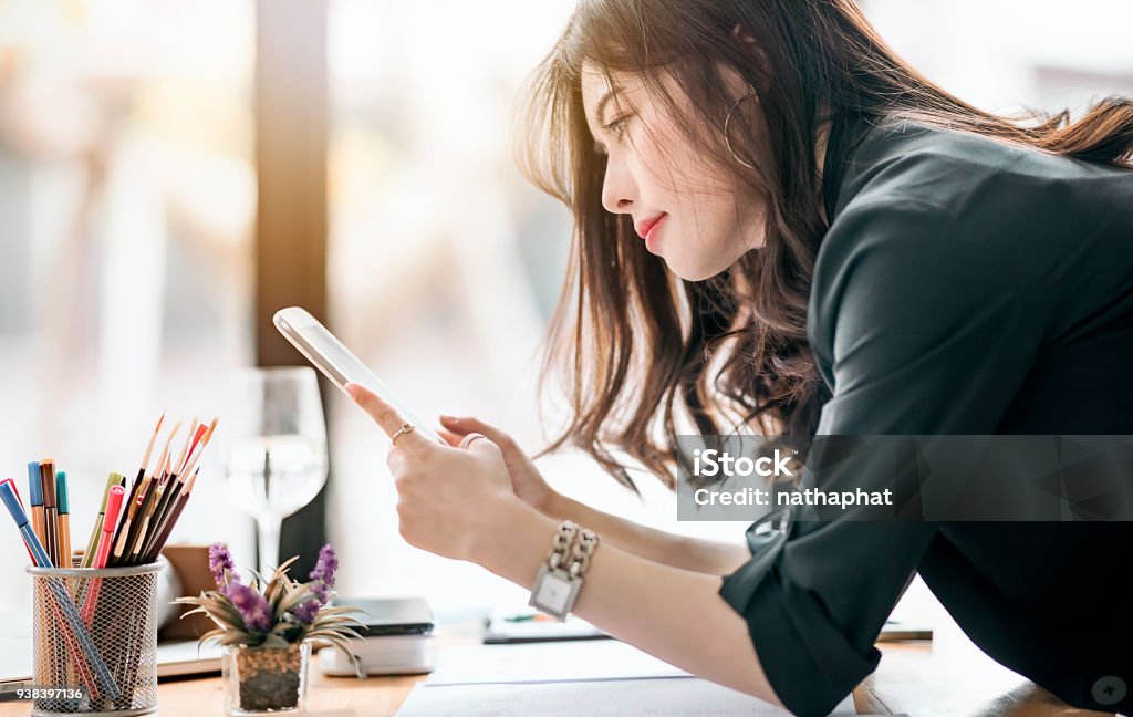 Rear view of beautiful female designer holding and looking at tablet screen Rear view of beautiful female designer holding and looking at tablet screen while working at modern office Digital Tablet Stock Photo