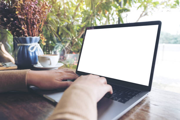 istock Mockup image of hands using and typing on laptop with blank white desktop screen on wooden table in cafe 938399528