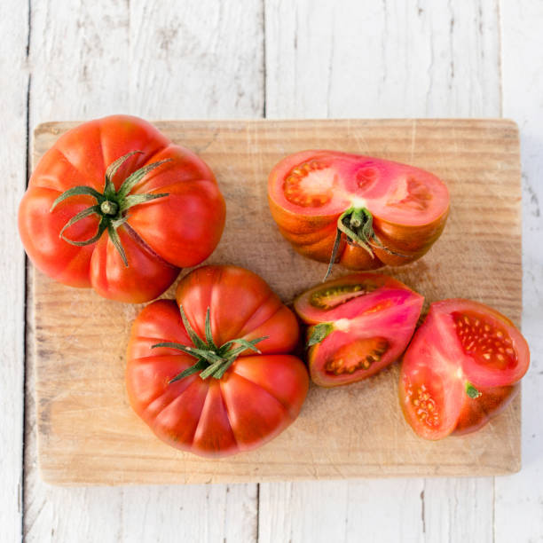 istock Raw delicious tomatoes  on cutting board on  old wooden table in rustic style, top view. Beefsteak tomatoes type 938401580