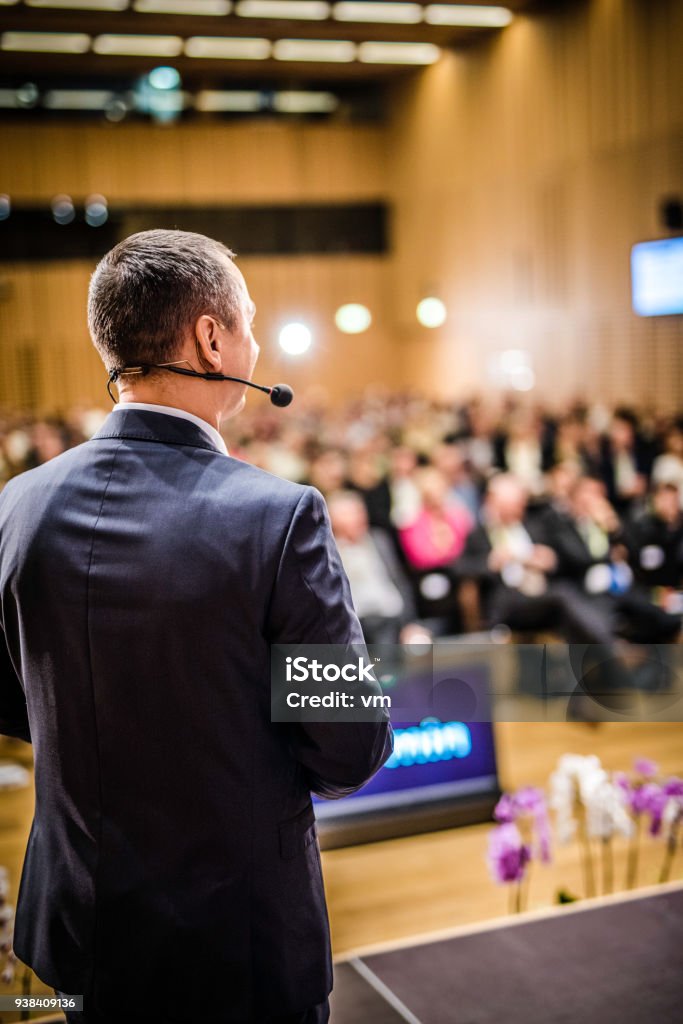 Rear view of a motivational coach giving a speech Rear view of a businessman entrepreneur giving a lecture to a sold-out crowd in a lecture hall. Conference - Event Stock Photo