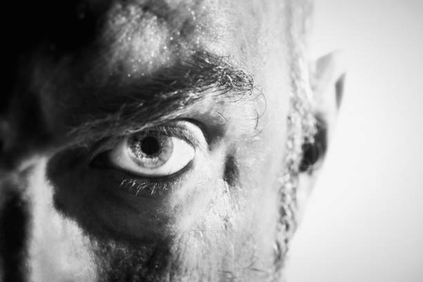 Threatening man glaring angrily in black-and-white close-up A cropped portrait in black and white of a mature man's face, frowning and glaring at camera in a threatening way. harassment photos stock pictures, royalty-free photos & images