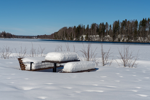 Bench and table in a park, covered with a thick layer of snow, on a beautiful sunny winter day in Sweden
