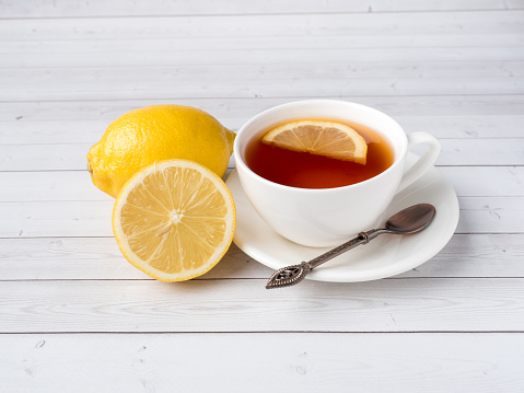 Herbal black tea in a white Cup, honey in a jar of fresh lemon on white wooden background.