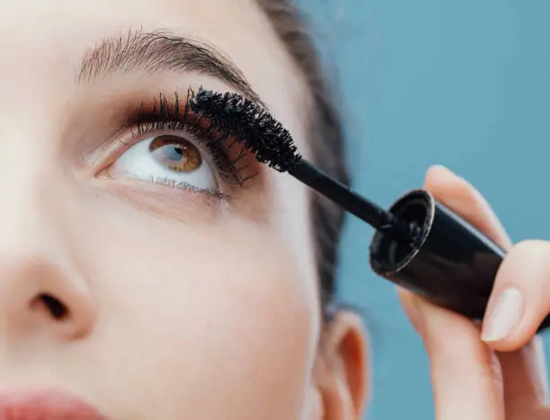 Woman applying mascara on her lashes, make up and cosmetics concept