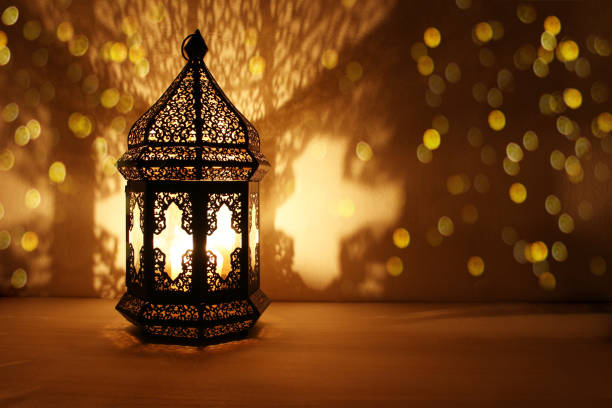 ornamental arabic lantern with burning candle glowing at night and glittering golden bokeh lights. festive greeting card, invitation for muslim holy month ramadan kareem. dark background - leste imagens e fotografias de stock