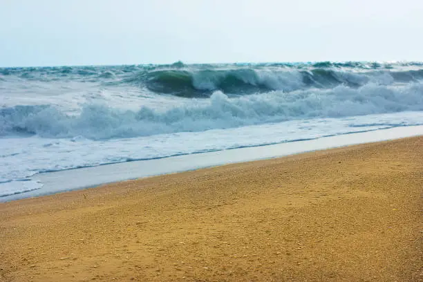 Photo of Stormy sea and blue sky, white sea foam on the yellow sandy beach.