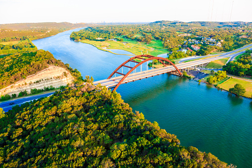 Panoramic aerial view from helicopter of 360 bridge on Colorado River near Austin Texas, looking east.\nAustin city skyline visible in far distance.
