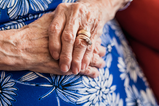 Senior woman sitting in an armchair in a  nursing home in North East of England. Close up of her hand and rings