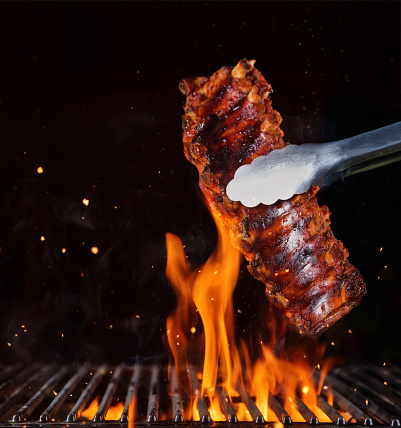 Pork ribs over flaming grill grid, isolated on black background. Barbecue and cooking
