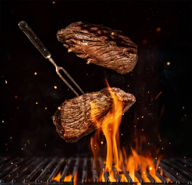 Flying beef steaks over grill grid, isolated on black background stock photo
