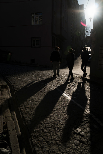 Istanbul, Turkey - March 15, 2018 : Silhouettes and shadows of three young men at the street of Istanbul, Balat District. They were walking on the cobblestone way between buildings.