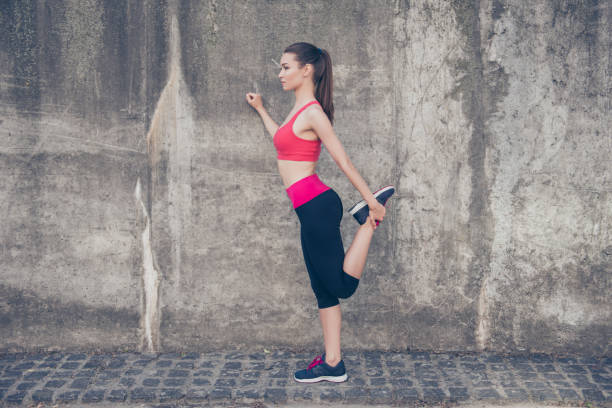 istock Pretty young slim trainer is stretching her legs by doing exercise. She is training outdoors on a summer day, wearing fashionable sport wear, focused 938477240