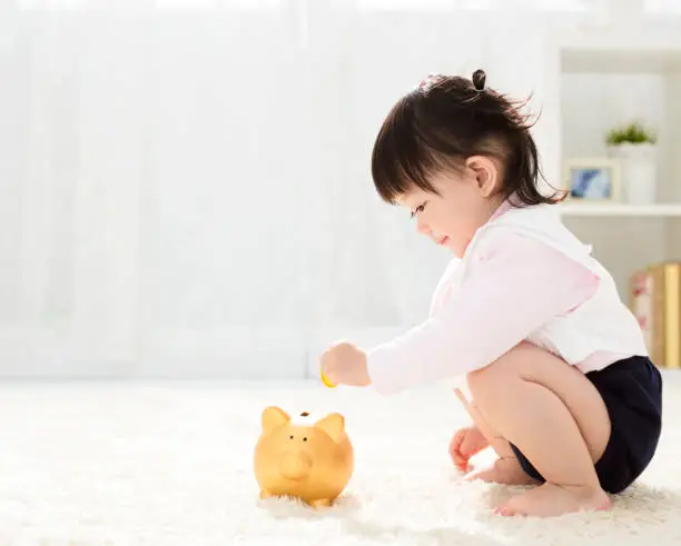 Photo of baby girl inserting a coin into piggybank
