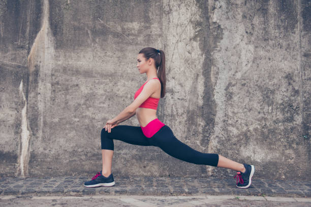 istock Pretty young slim trainer is stretching her legs by doing exercise. She is training outdoors on a summer day, wearing fashionable sport wear, focused 938480534