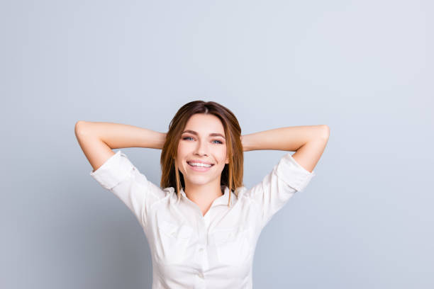 istock Time to rest. Young freelancer with beaming smile is relaxing, hands behind the head, dreaming and enjoying, in white shirt on pure background 938502514