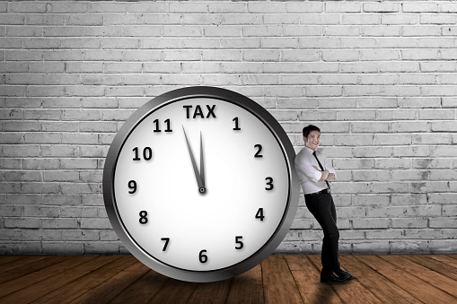Attractive asian businessman lean back on the clock with tax deadline. Goods and Services Tax concept.