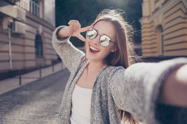 kaygısız ve mutlu, güneşli bahar ruh hali. sevimli genç gülümseyen kız selfie açık havada yürürken bir kamera haline getiriyor. gündelik kıyafet, ayna gözlük takıyor - güneş videolar stok fotoğraflar ve resimler