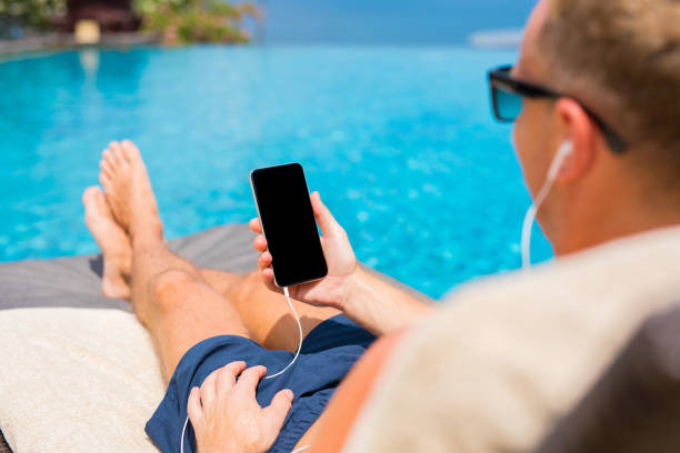 homme à l’écoute de la musique sur le téléphone de la piscine - tourist resort audio photos et images de collection