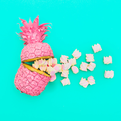 two painted in pink color halfs of the pineapple of which fall marshmallow on turquoise background. fashion minimalism concept of summer food. surreal