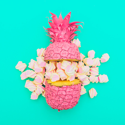 two painted in pink color halfs of the pineapple of which fall marshmallow on turquoise background. fashion minimalism concept of summer food. surreal. flat lay