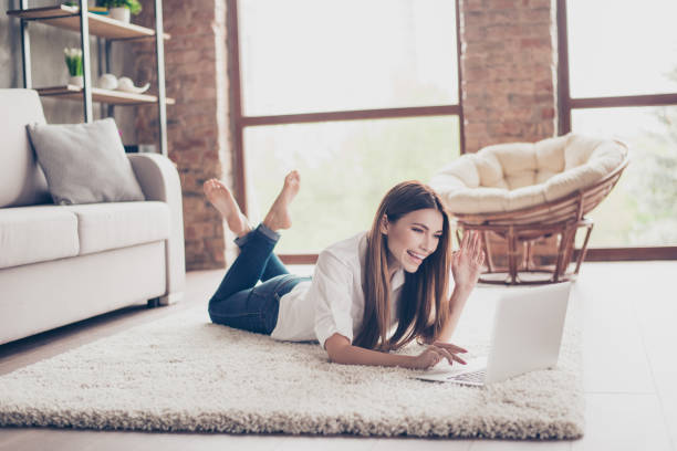 istock Hello there! Young cheerful lady is waving to the camera while having video call lying on the carpet at home, so happy and excited 938512230