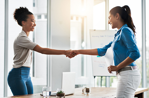 Shot of two young businesswomen shaking hands in a modern office