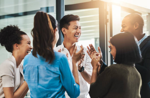 Nothing motivates productivity like team morale Shot of a group of young businesspeople standing together and clapping in a modern office coworker stock pictures, royalty-free photos & images