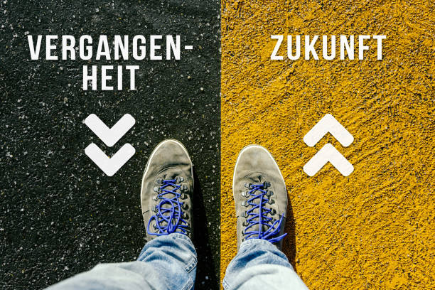 Concept of facing a crucial decision symbolized by vergangenheit and zukunft in german meaning past and future written on different colored pathways Reaching a crossroads having to choose between vergangenheit and zukunft meaning past and future symbolized by two feet standing on two different colors with arrows on pathway from above zukunft stock pictures, royalty-free photos & images