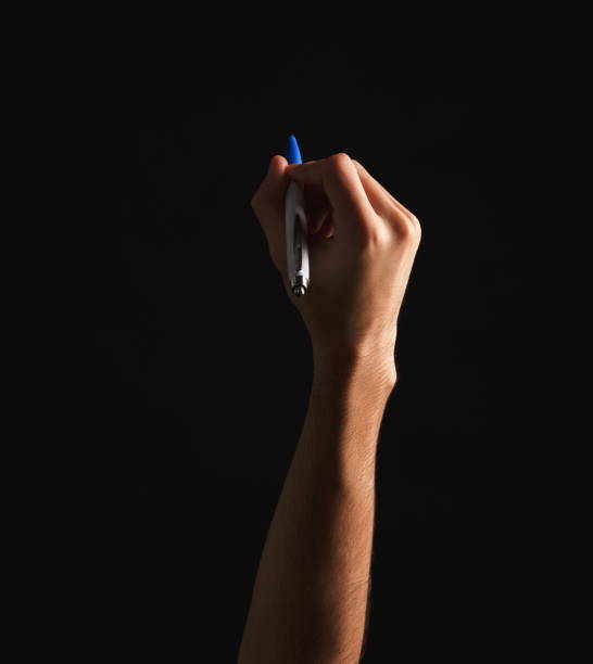 istock Male hand holding pen isolated on black 938521188