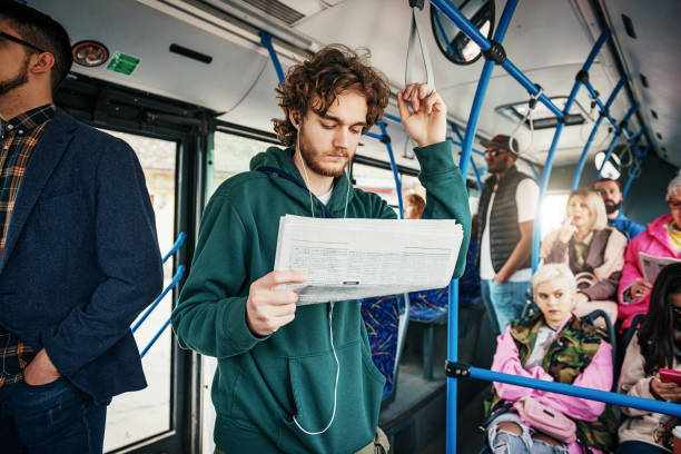 Youth reading classified ads and searching for a job while traveling by public bus, while others going to work