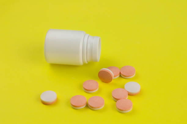 istock Scattered double color whole pills beside empty plastic container on background of yellow paper 938524542